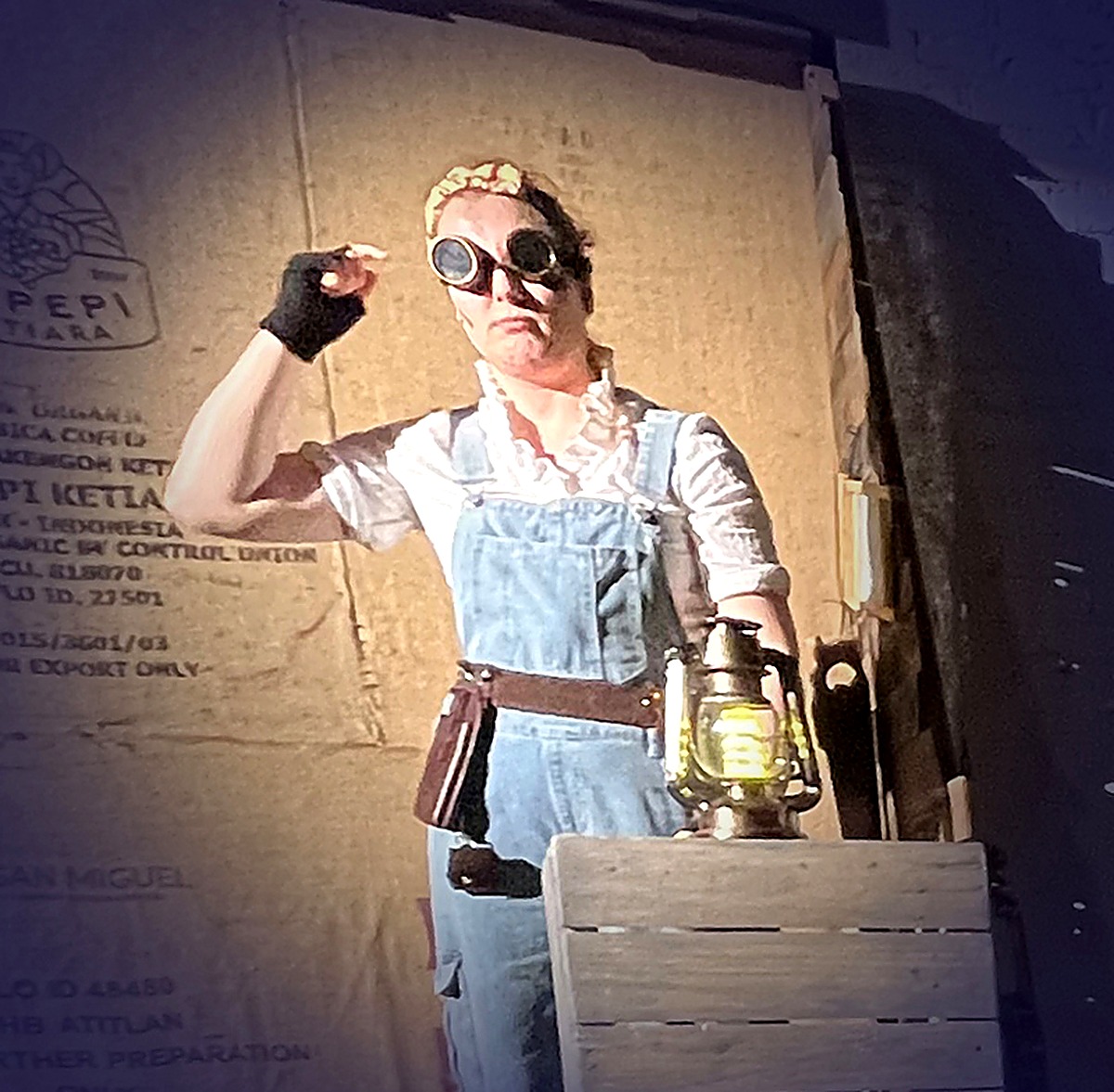 The Woodcarver, her face clearly visible, wearing overalls and goggles and holding a glowing lantern